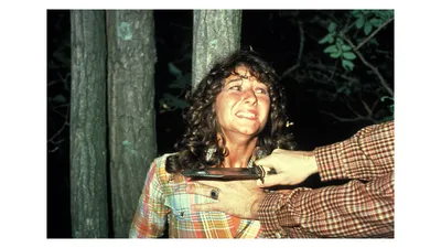Medium Shot of Robbi Morgan as Annie standing against a tree with a knife at her throat.