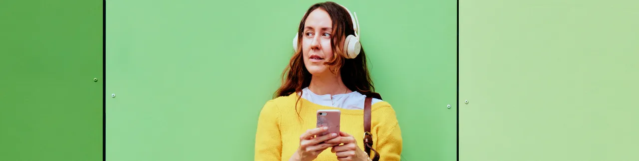 Kvinna med hörlurar och mobil framför sig. 