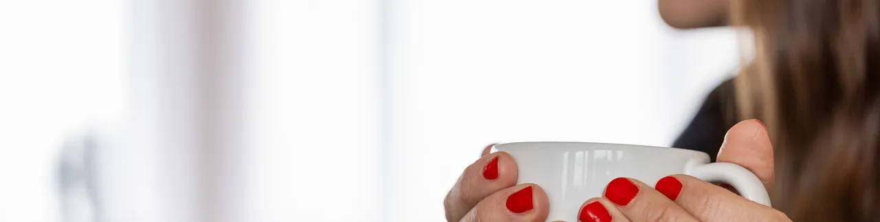 Kvinna i profil håller i vit mugg. rött nagellack. 